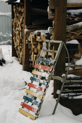 Vintage sled stand against the background of the snow-covered firewood under a canopy