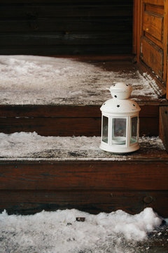 white lantern on theon the snow-covered porch. wooden staircase to the house. Beautiful winter background, copy space