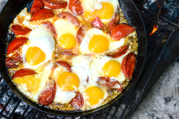 Scrambled eggs with tomatoes is prepared on a black pan on a metal lattice in the journey. The concept of the dish: a combination of protein and fiber. The view from the top