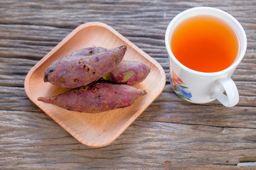 A cup of tea and red sweet potato on wooden plate over rustic wooden table