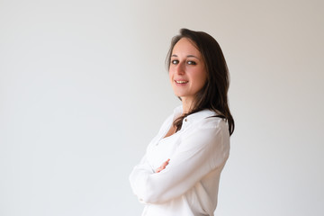 Smiling confident girl in white shirt posing with arms crossed. Side view of beautiful young woman...