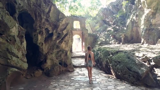 backside girl walks through gate in stone arch from cave
