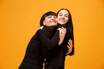 A portrait of a happy mother and daughter at studio on gold background. Trendy colors. Human positive emotions and facial expressions concept