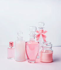 Variety of pink cosmetic product bottles and  flowers standing on white pink background with bokeh. Skin care, cosmetic shop, sale and abstract beauty concept.