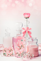 Variety of cosmetic product bottles with roses essence standing on white pink background with bokeh. Skin care, cosmetic shop, sale and abstract beauty concept