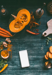 Smartphone with blank white screen mock up on kitchen tables with pumpkin and cooking ingredients, top view. Blog, online shopping, recipes concept