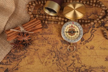 Fototapeta na wymiar Vintage compass with spyglass telescope and cinnamon spices on an old world map - trade and explorer concept