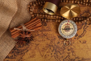 
Vintage compass with spyglass telescope and cinnamon spices on an old world map - trade and explorer concept