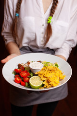 A waitress in a white shirt is holding a delicious salad.