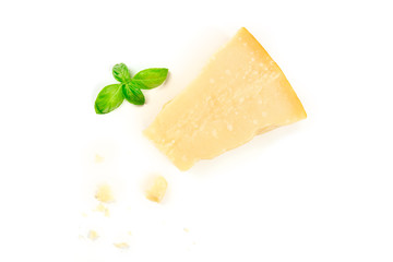A piece of aged Parmesan cheese with crumbs, shot from above on a white background with fresh basil leaves and a place for text