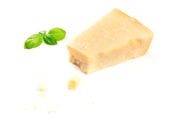 A piece of aged Parmesan cheese with crumbs on a white background with fresh basil leaves and copy space