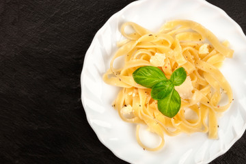 A closeup photo of a plate of Italian pasta with Parmesan cheese and fresh basil leaves, shot from above on a dark background with a place for text