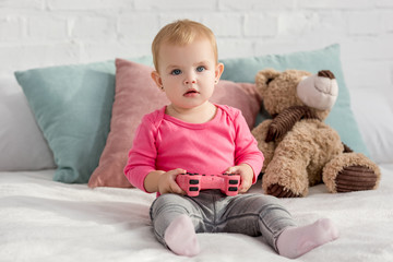 adorable child in pink shirt holding pink joystick on bed in children room