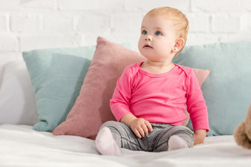 adorable kid sitting on bed with pillows and looking up in children room