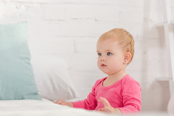 Naklejka premium adorable kid leaning on bed and looking away in children room