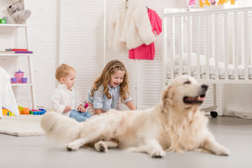 selective focus of adorable sisters playing on floor, golden retriever lying near in children room