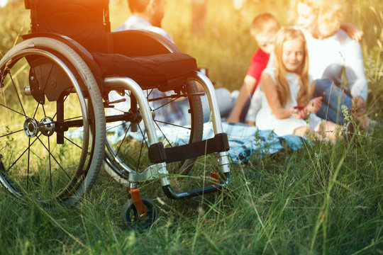 Focus on emply wheelchair on the foreground while happy family rest on the background