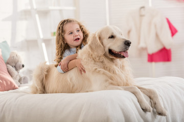 adorable kid and dog lying on bed in children room