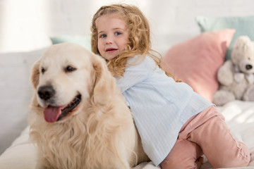 adorable kid and cute dog lying on bed in children room, looking at camera