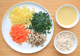 Chopped vegetables with soup and pork on white plate against wooden board background.