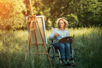 Woman in wheelchair drawing on easel outside
