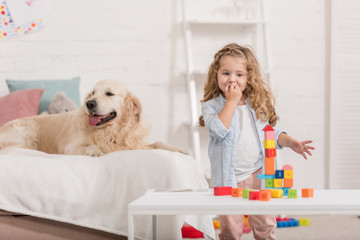 adorable child playing with educational cubes, golden retriever lying on bed in children room