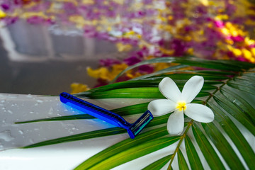 Razor on palm leaf with white tropical flower plumeria on a bath with flower petals sea beach.epilation and depilation removal of unwanted hair from the body spa and female beauty bikini area concept