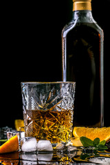 Still life with cognac glass and bottle, orange fruit snack on a black background. copy space