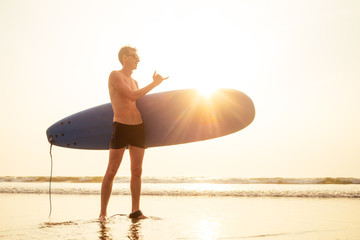 shaka hand gesture surfers symbol.young surfer man with surfboard on the beach summer sunset...