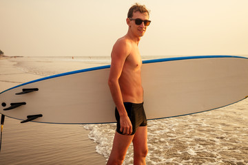 male athlete surfer running to the sea with surf board sunset at the beach tropical paradise...