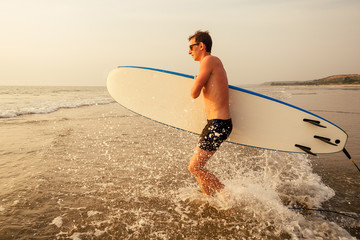 male athlete surfer running to the sea with surf board sunset at the beach tropical paradise...
