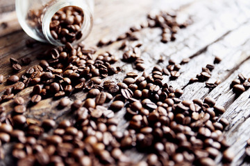 Coffee beans are on the wooden textured table with the glass jar.