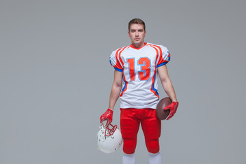 American football player holding rugby ball and helmet against grey background front view © satyrenko