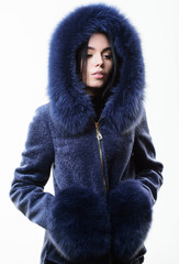 Fashion concept. Girl elegant lady wear fashionable coat jacket with furry hood. Luxurious fur. Girl posing hooded fur coat. Female with makeup wear dark blue soft fur coat. Woman wear hood with fur