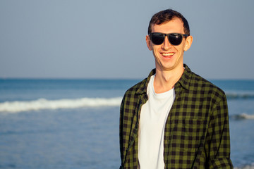 Cheerful young man in plaid green shirt over white t-shirt standing on the beach