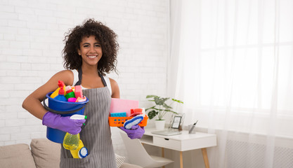 Smiling black woman posing with cleaning supplies