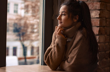 Portrait of young gorgeous female  thoughtfully looking out of the coffee shop window while enjoying her leisure time alone, nice business woman lunch in cafe during her work break