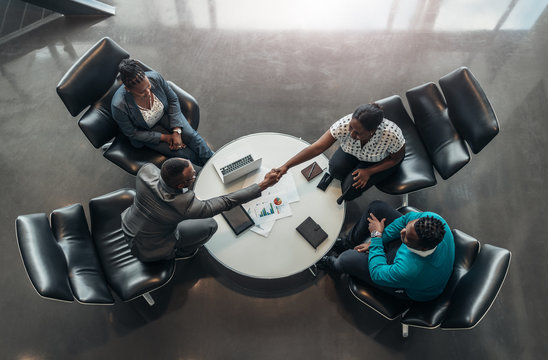 Group of African business people sitting and discussing statistics during a sit down meeting taking from above. Two colleagues are shaking hands