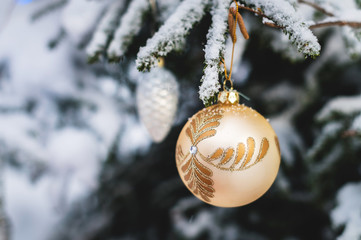 Close-up of a Christmas toy on a snow-covered lively tree in the winter forest on the background of lights