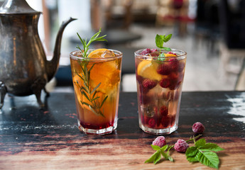 Tea in glasses on the old table against the background of a cafe and vintage teapot. Sai with orange and rosemary and tea with lemon, raspberry and mint