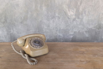 Vintage telephone on wooden table with cement wall background, image with copy space.
