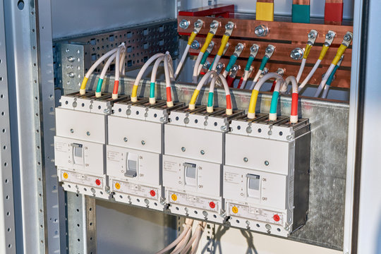 The electrical wires or cables are connected to the circuit breakers. In the background, copper busbars are visible in the electrical Cabinet. Production technology of electrical cabinets.