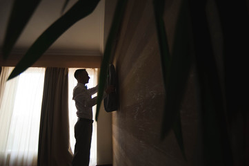 Groom getting ready in the morning before wedding ceremony, putting on jacket on shirt in room.