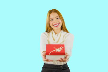 Fototapeta na wymiar Portrait of a beautiful young red-haired girl who smiles at the camera and demonstrates a box with a gift, gives for a birthday, isolated background