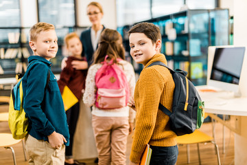 schoolboys with books and backpacks looking at camera in library