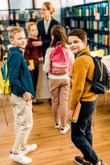 boys with books and backpacks looking at camera in library
