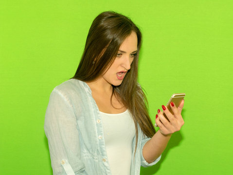 Portrait angry young woman screaming on mobile phone, Isolated on a green background. Negative emotions feelings