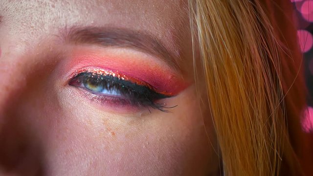Closeup of charming female blue eyes makeup with pink shades and gold eyeline looking on theleft and then straight at camera