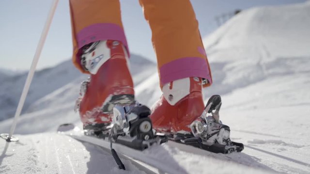 4K winter sport footage, close up female skier woman stepping in ski binding strap on skies on piste skiing away on sunny winter day in mountains with snow