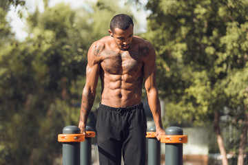 Athletic naked man doing push ups on parallel bars